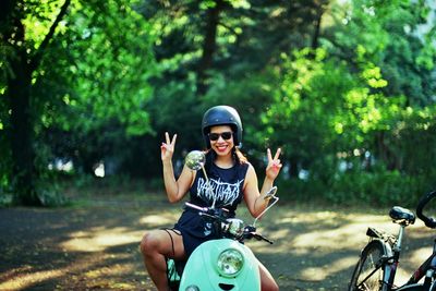 Happy woman in sunglasses sitting on motor scooter showing peace sign