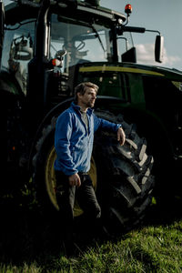 Contemplative farmer standing by tractor at farm