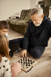 Smiling grandfather playing chess with grandchildren at home