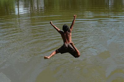 High angle view of playful shirtless man jumping in lake