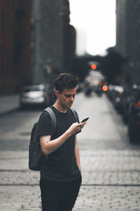 Young man using mobile phone while standing on street in city