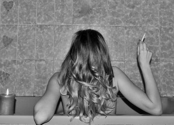 Rear view of shirtless woman smoking cigarette in bathtub