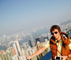 Male tourist listening music on mobile phone while standing at observation point by cityscape