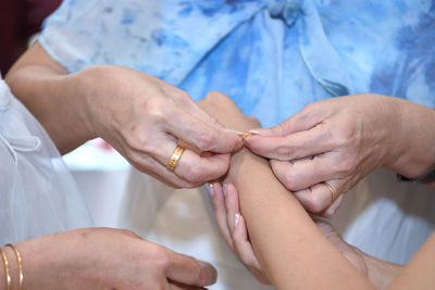 Midsection of woman putting bracelet in friend hand at home