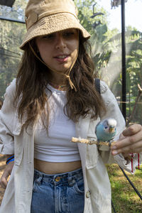 Beautiful young woman feeding a bird with a wooden stick with seeds stuck to it, bird stops to eat