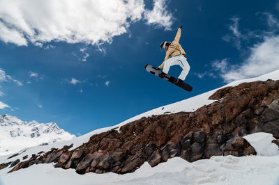 Professional snowboarder jumps high into the air from the kicker, taking the board with his hand