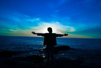 Rear view of silhouette man standing by sea against sky