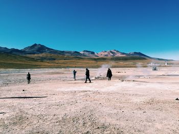 People on desert against clear blue sky