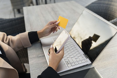 Businesswoman with smart phone and laptop paying through credit card