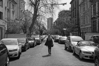 Rear view of woman walking on street by parked cars in city