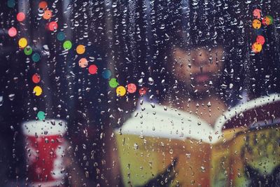 Woman reading book seen through wet glass window