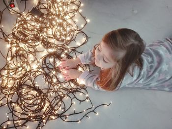High angle view of girl with illuminated string lights on floor