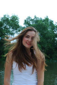 Portrait of beautiful young woman standing against lake in park
