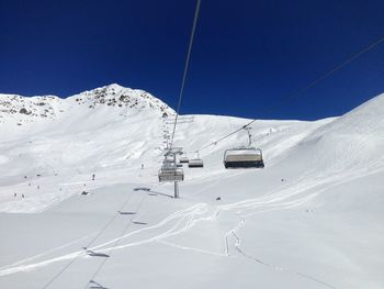 Ski lifts over snow covered field against clear blue sky