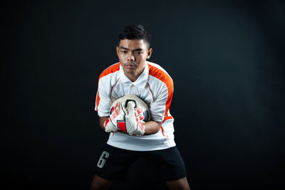 Portrait of young man standing against black background