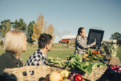 Farmers looking at instructor writing on blackboard with organic vegetables for sale at market