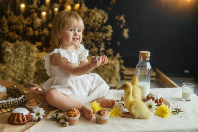 A little girl is sitting on the easter table and playing with cute fluffy ducklings. happy easter.