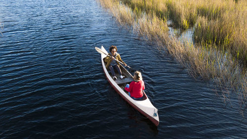 Man with oar paddling while sitting with woman in canoe on river