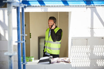 Architect talking on mobile phone while standing at incomplete building