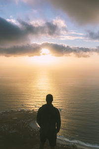 Rear view of man looking at sea against sky during sunset