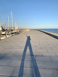 Shadow of man on pier at harbor against clear sky