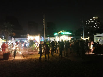 People at beach against sky in city at night