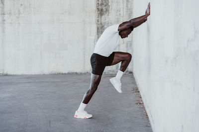 Sportsman doing stretching workout while leaning on white wall