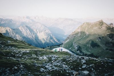 Hikers on cliff by mountains against clear sky