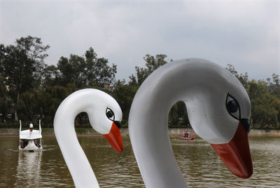 Artificial swans by lake against sky