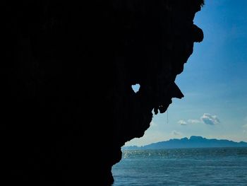 Silhouette rock formation in sea against sky