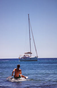 Rear view of man paddleboarding in sea against clear sky