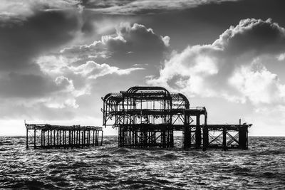 Silhouette damaged west pier amidst sea against cloudy sky