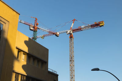 Low angle view of crane by building against sky