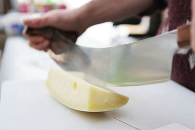 Cropped hands cutting cheese on table