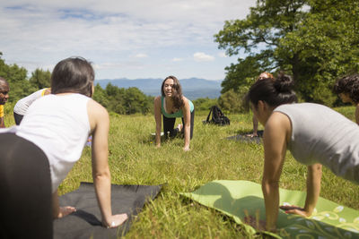 Friends practicing downward facing dog position while exercising on field