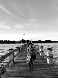 Woman walking on pier over sea against sky