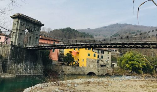 Bridge over river by buildings against sky