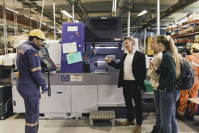 Businessman and family discussing with male worker while standing by manufacturing machinery in factory