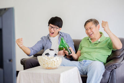 Father and son clenching fists while watching sport at home