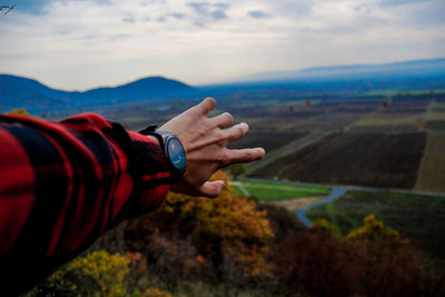 Cropped hand of man reaching landscape against sky