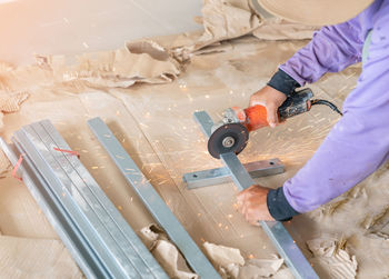 A male hand without gloves cuts off pieces of steel bar using an angle grinder.