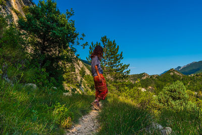 Woman walking by plants against blue sky