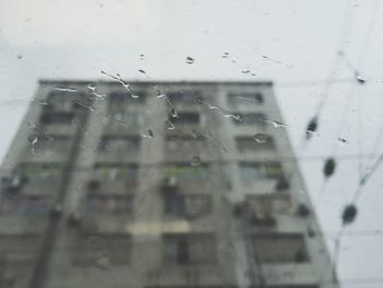 Low angle view of building seen through wet glass