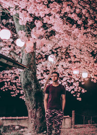 Thoughtful young man standing by illuminated tree at night