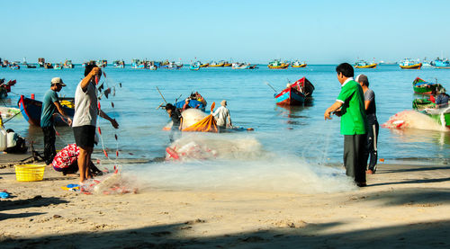 Fishermen pulling net out of sea against clear blue sky