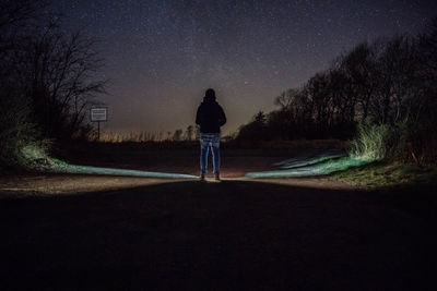 Rear view of man standing on road at night