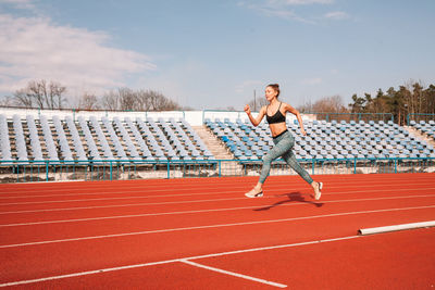 Full length of woman running on track against sky