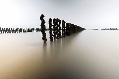 Reflection of wooden posts in lake against sky