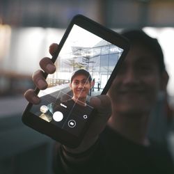 Portrait of man holding smart phone seen on device screen outdoors