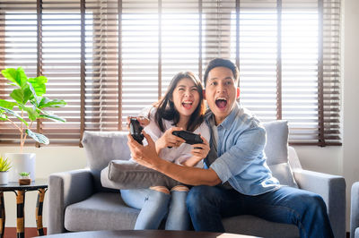 Smiling couple playing video game while sitting on sofa at home